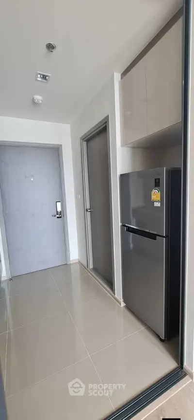Modern apartment entryway with sleek refrigerator and glossy tile flooring.