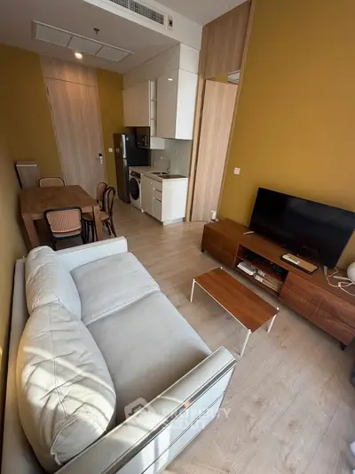 Modern living room with cozy sofa, dining area, and compact kitchen featuring washing machine and TV setup.