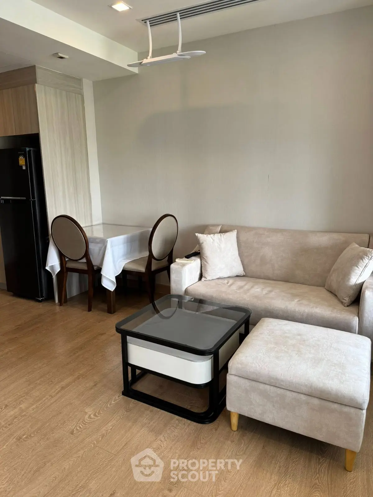 Modern living room with cozy beige sofa, elegant dining area, and sleek black refrigerator.