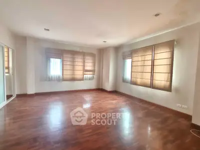 Spacious empty room with wooden flooring and large windows, perfect for customization.