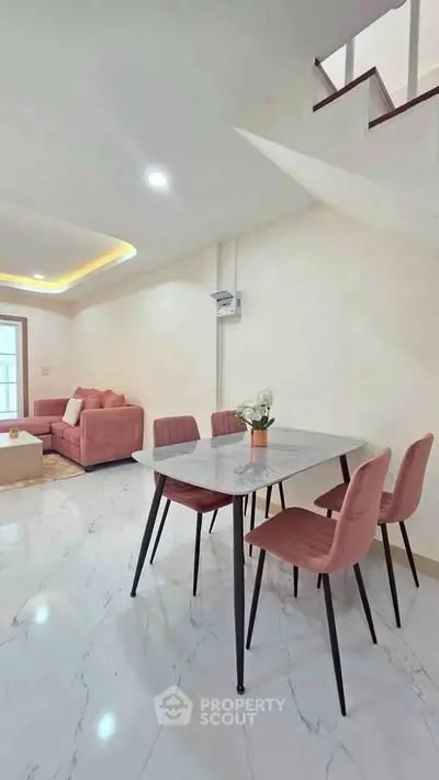 Modern living room with stylish dining area and elegant staircase, featuring pink chairs and marble flooring.
