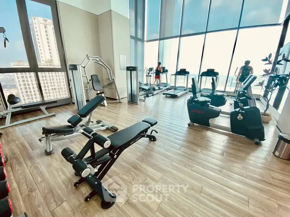 Spacious modern gym with city view in luxury high-rise building.