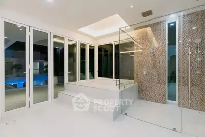 Luxurious modern bathroom with glass shower and large windows overlooking pool area.