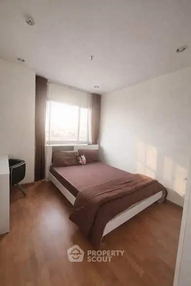 Cozy bedroom with wooden flooring and large window offering natural light.