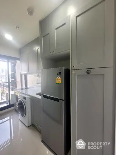 Modern kitchen with sleek cabinetry, fridge, and washing machine in a bright apartment.