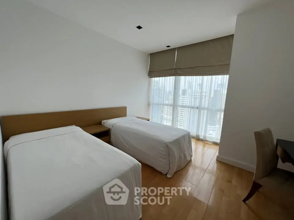 Spacious bedroom with twin beds and city view, featuring modern decor and natural light.