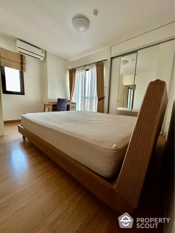 Spacious bedroom with modern design and natural light, featuring wooden flooring and mirrored wardrobe.