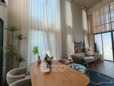 Spacious living room with high ceilings and elegant decor, featuring large windows and stylish furniture.