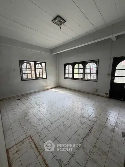 Spacious empty room with tiled flooring and arched windows, ideal for customization.