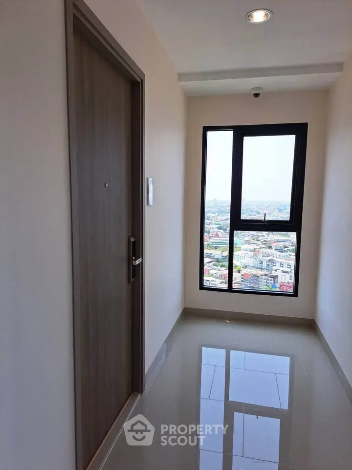 Modern apartment corridor with city view through large window, sleek door, and polished floor.