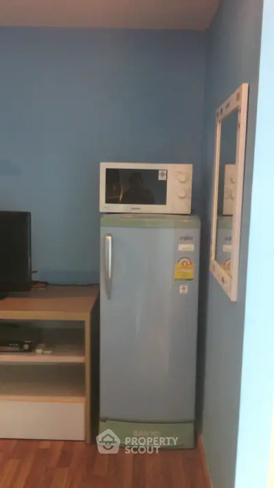 Compact kitchen corner with fridge, microwave, and TV stand in cozy apartment.