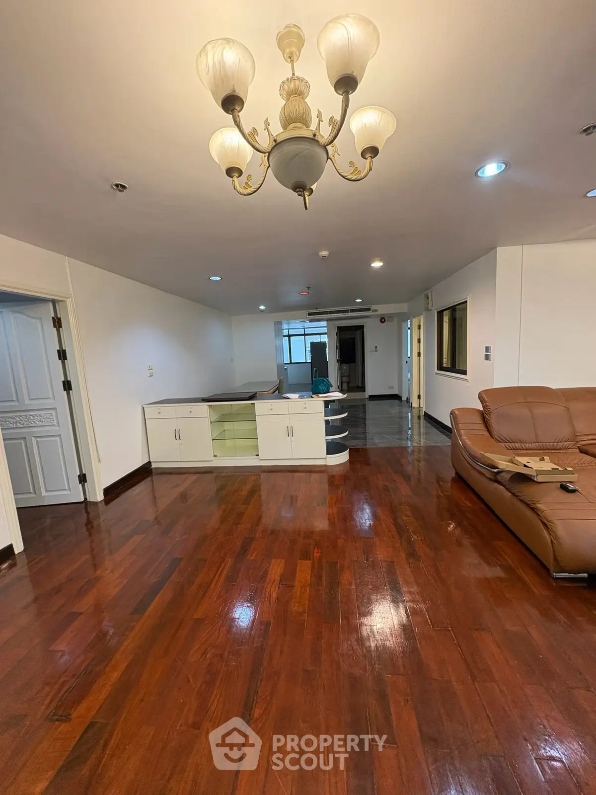 Spacious living room with elegant chandelier and polished wooden floors in modern apartment.