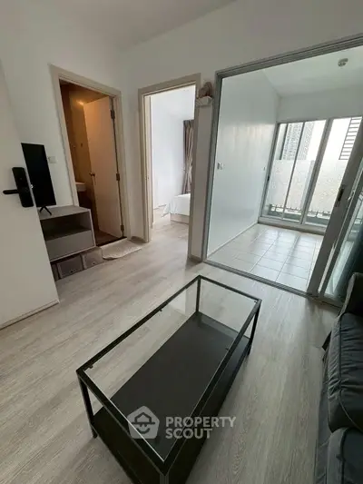 Modern apartment interior with glass coffee table and sliding doors leading to a balcony.
