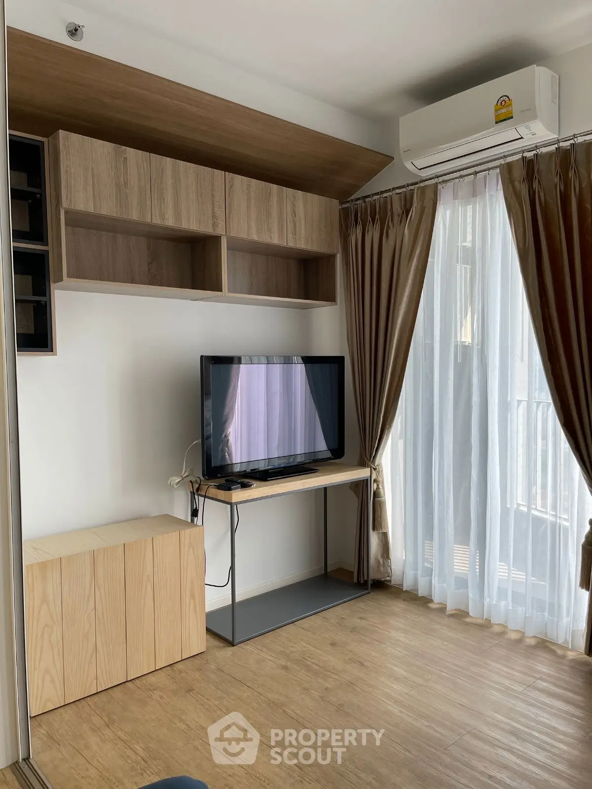 Modern living room with TV, wooden flooring, and elegant curtains in a cozy apartment.