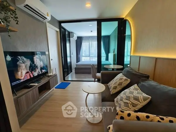 Modern living room with cozy sofa and TV, open view to bedroom