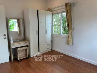 Spacious bedroom with wooden flooring and ample natural light from large window.