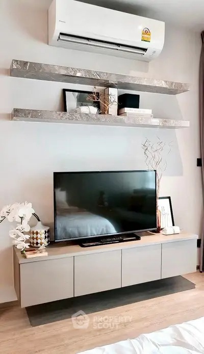 Modern living room with sleek TV unit and stylish floating shelves under air conditioning unit.
