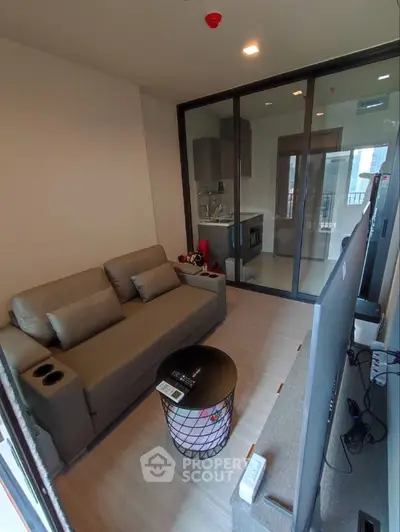 Modern living room with sleek furniture and glass partition leading to a compact kitchen.