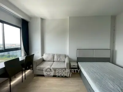 Modern studio apartment with cozy sofa and bed, featuring large window with city view.