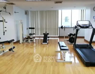 Spacious gym with modern equipment and wooden flooring in a bright room.