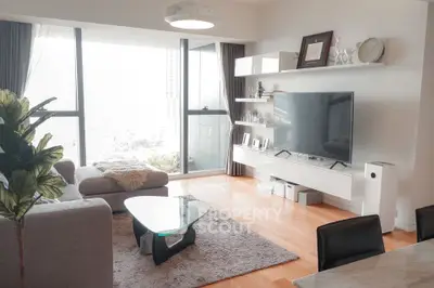 Modern living room with large TV, stylish furniture, and floor-to-ceiling windows offering a bright ambiance.
