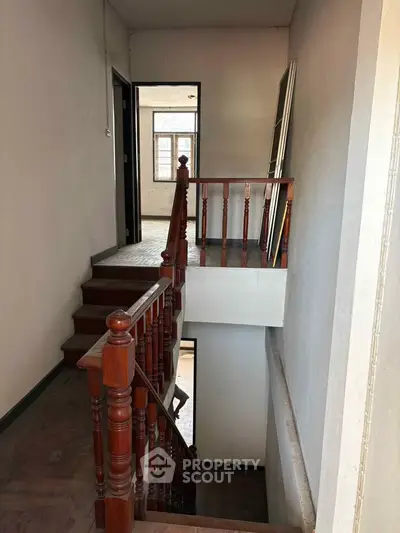 Charming staircase with wooden railing in a cozy home interior, offering a glimpse of natural light through the window.
