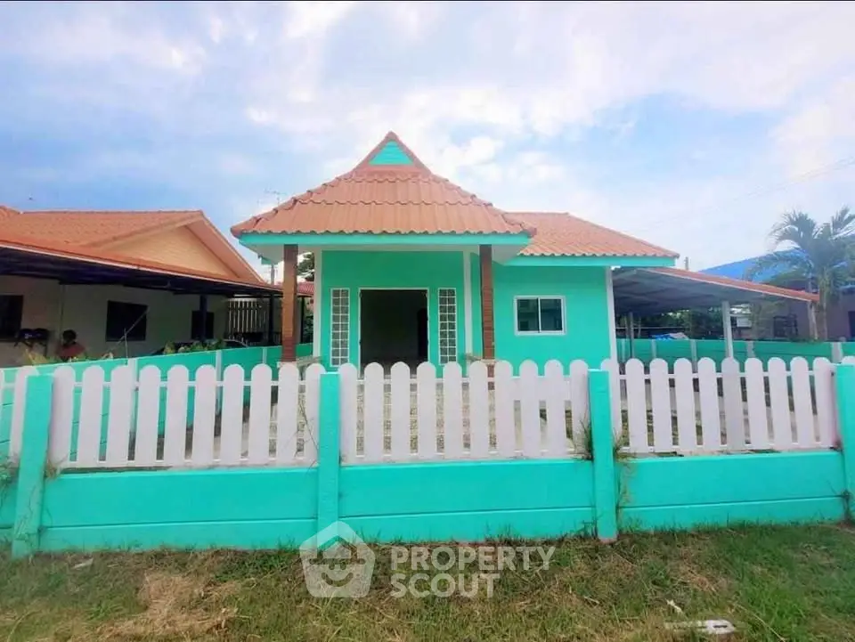 Charming turquoise house with white picket fence and terracotta roof, perfect for family living.
