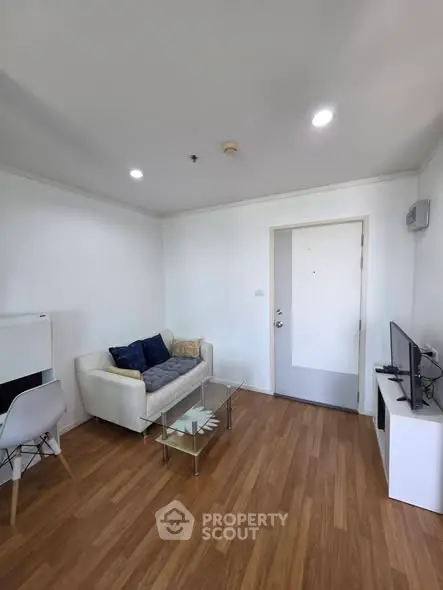 Modern living room with wooden flooring, cozy sofa, and sleek TV setup in a bright apartment.