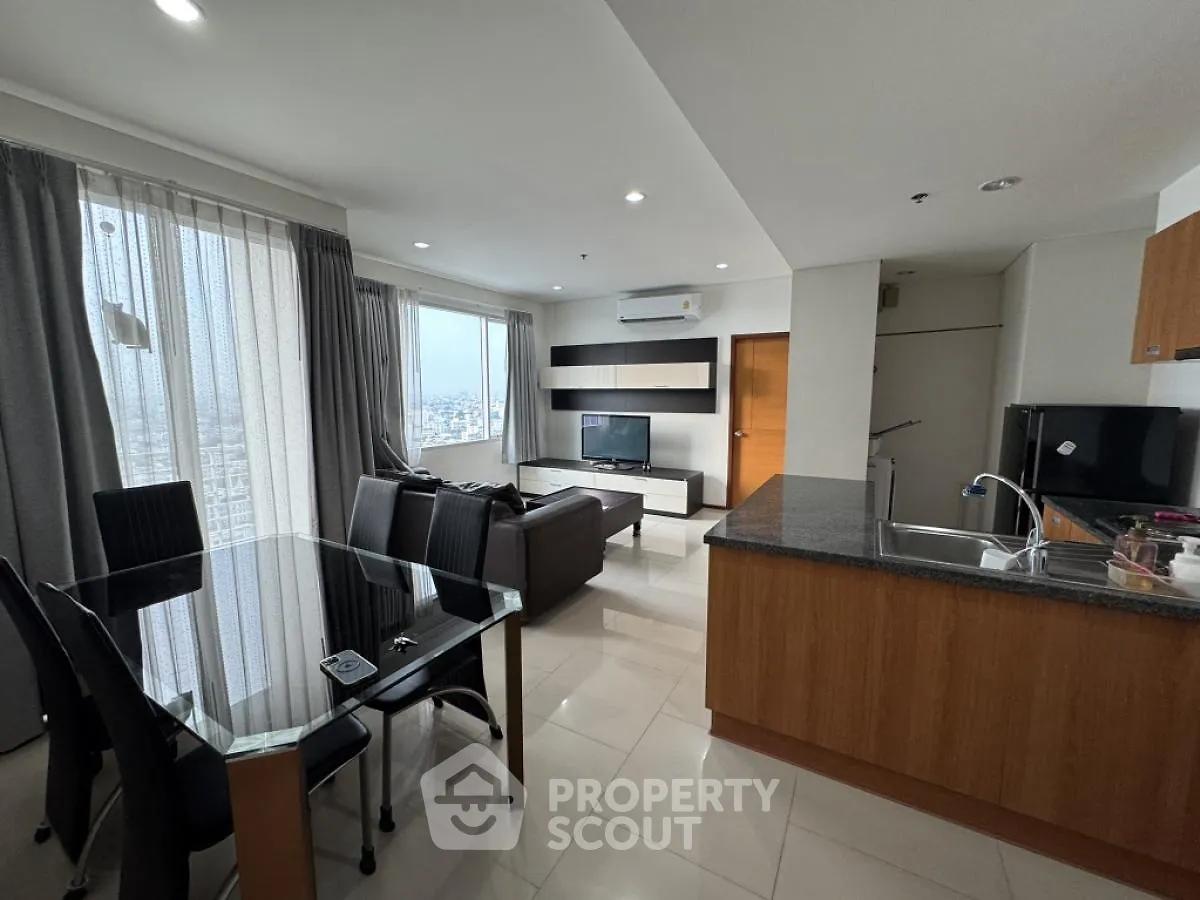 Modern open-layout living room with dining area and kitchen, featuring sleek furniture and large windows.