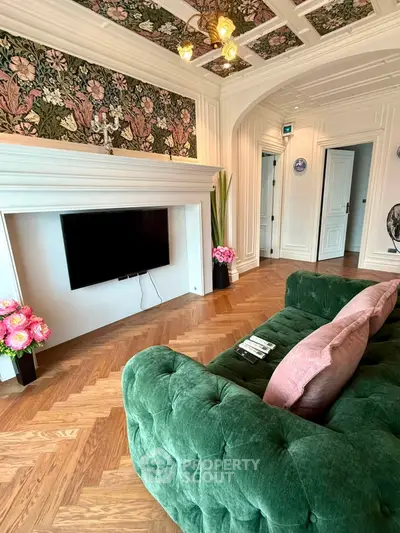 Luxurious living room with elegant decor and plush green sofa, featuring a wall-mounted TV and intricate ceiling design.