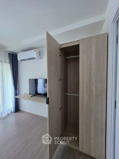 Modern living room with air conditioning and wooden wardrobe, featuring a sleek TV setup.
