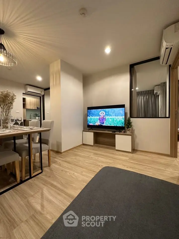 Modern living room with stylish decor and open dining area, featuring a mounted TV and elegant lighting.
