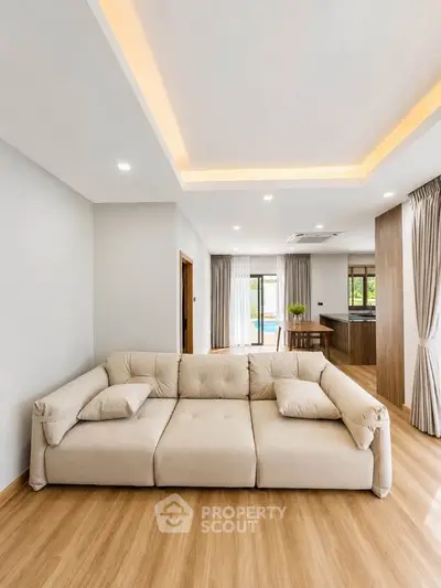 Spacious modern living room with elegant beige sofa and open layout, featuring natural light and wooden flooring.