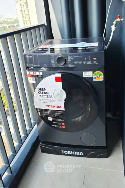 Modern Toshiba washing machine on a high-rise balcony with city view, perfect for urban living convenience.