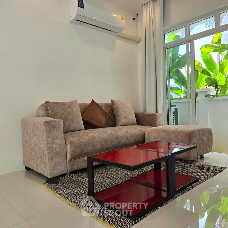 Modern living room with stylish sofa and glass coffee table, featuring a lush garden view through large windows.