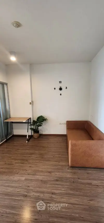 Spacious living room with modern decor and stylish wall clock, featuring a cozy brown sofa and sleek wooden flooring.