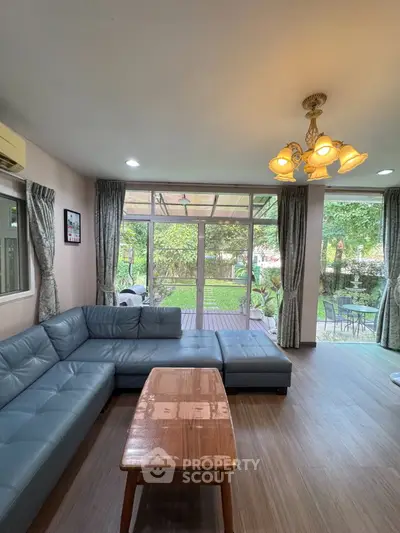 Spacious living room with large windows and garden view, featuring a stylish sectional sofa and elegant lighting.