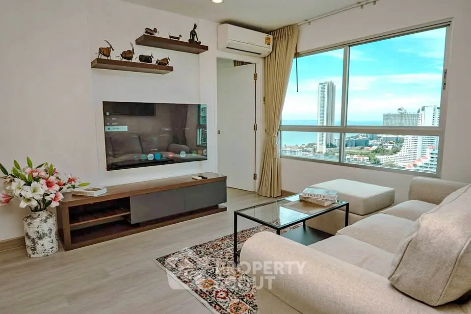 Modern living room with large window offering stunning city and ocean views, featuring cozy sofa and stylish decor.