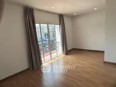 Spacious living room with gleaming hardwood floors and large windows leading to a sunny balcony, perfect for entertaining or relaxation.