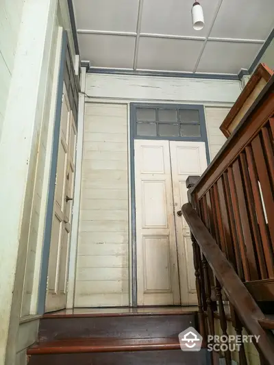 Charming vintage staircase leading to a classic wooden door, featuring traditional railings and a transom window, exuding old-world elegance.