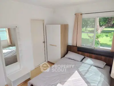 Cozy bedroom with natural light and park view, featuring a bed, wardrobe, and vanity mirror.