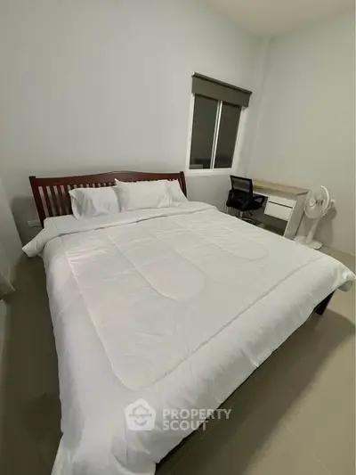 Cozy bedroom with large bed, desk, and fan, perfect for relaxation and work.