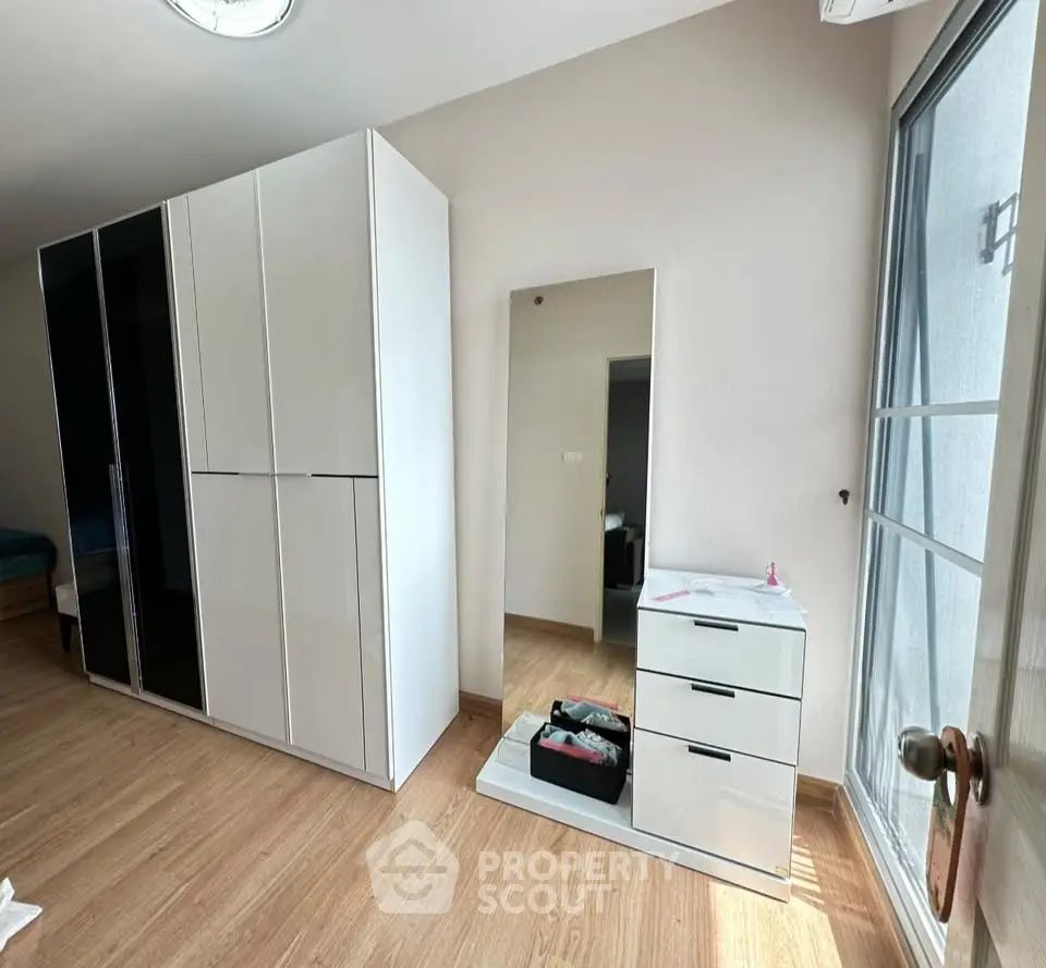 Spacious bedroom with modern white wardrobe and dresser, featuring natural light from large window.