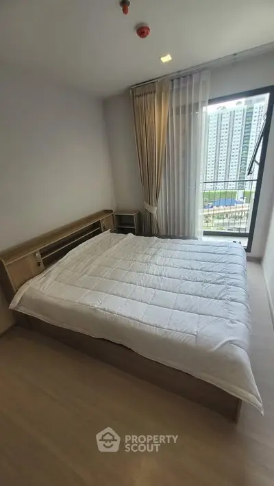 Modern bedroom with large window and city view, featuring a cozy bed and stylish curtains.