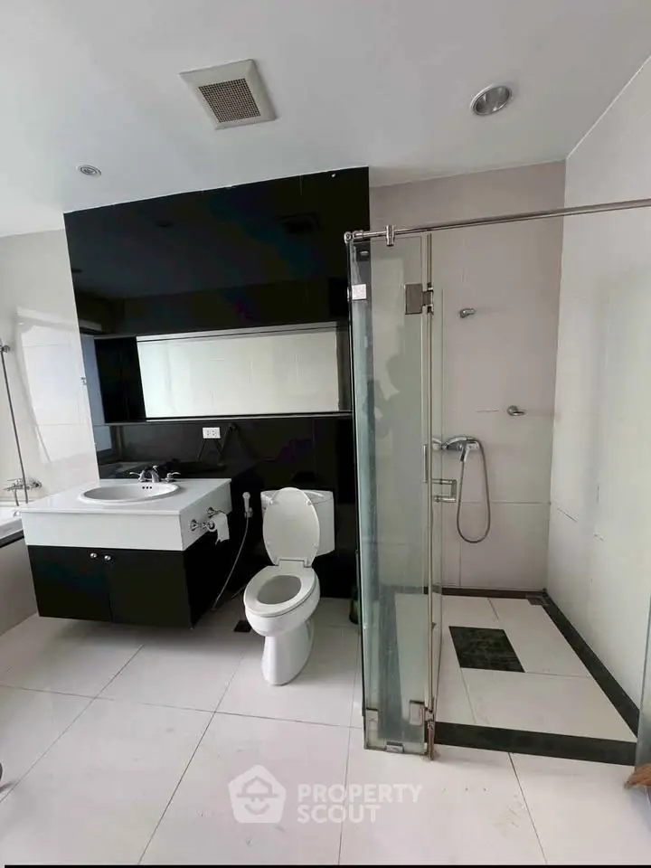 Modern bathroom with sleek black and white design, featuring a glass shower and stylish vanity.
