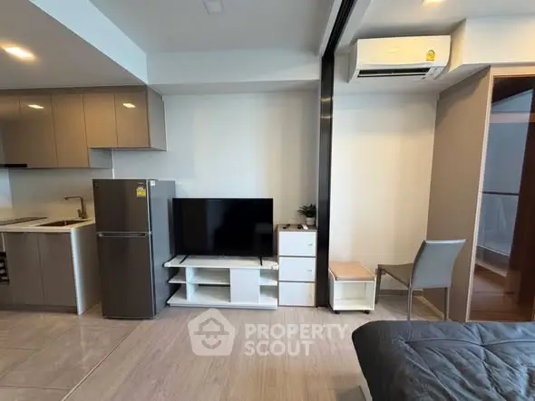 Modern studio apartment with sleek kitchen and cozy living area, featuring a TV and air conditioning.
