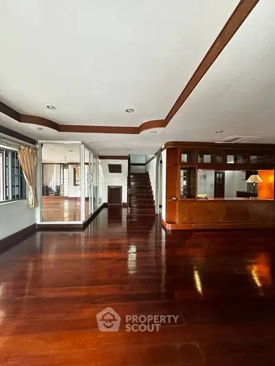 Spacious living room with polished wooden floors and elegant staircase in luxury home.