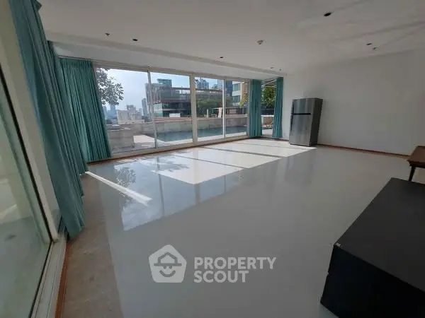 Spacious living room with large windows and city view, featuring a modern refrigerator.