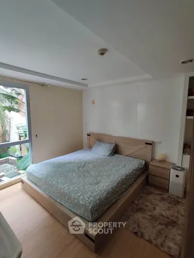 Cozy bedroom with modern decor and large window offering natural light and garden view.