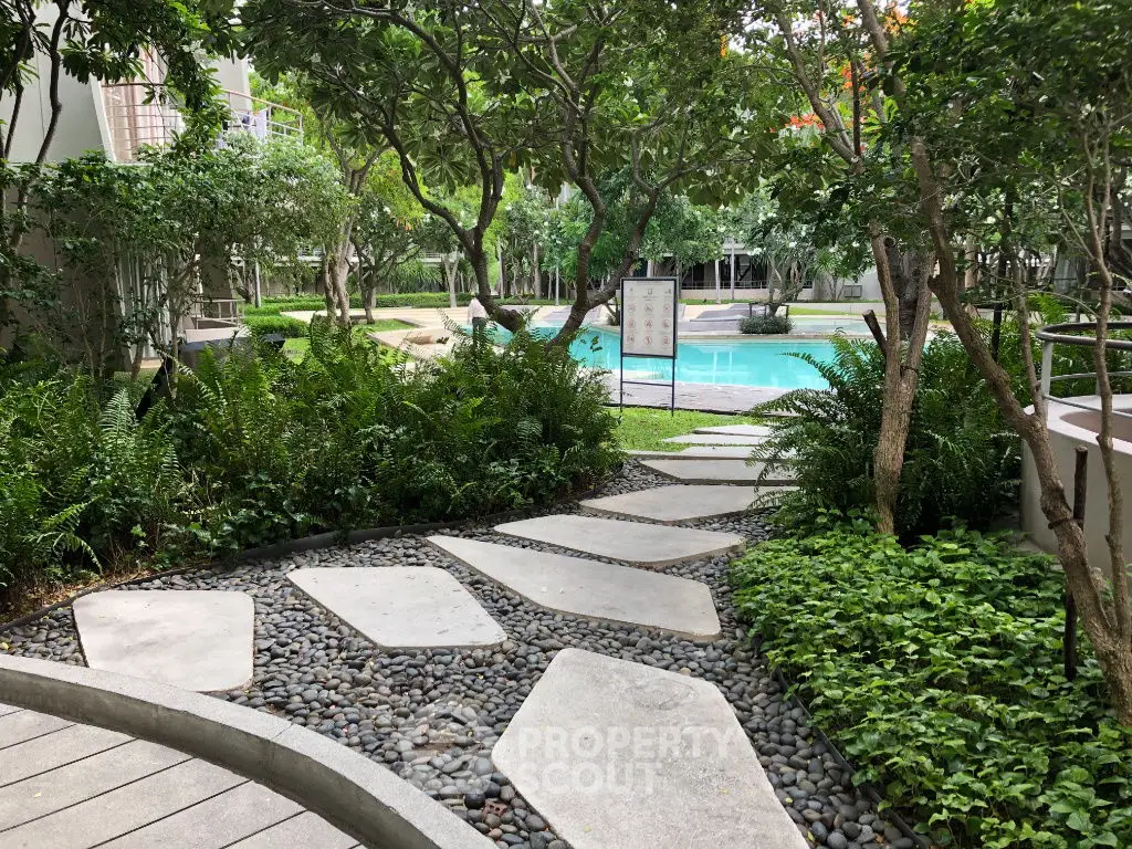 Lush garden pathway leading to a serene pool area in a modern residential complex.